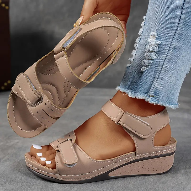 Beige sandals worn with ripped jeans on a neutral background