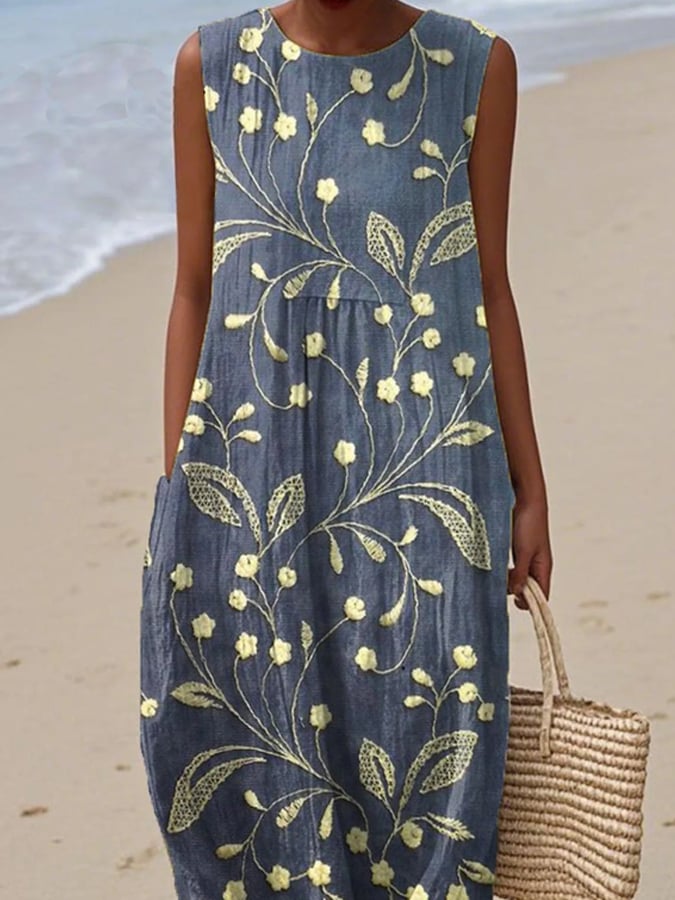 Woman wearing a blue dress with yellow floral patterns on a beach.