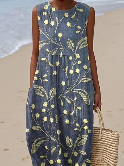 Woman wearing a blue dress with yellow floral patterns on a beach.