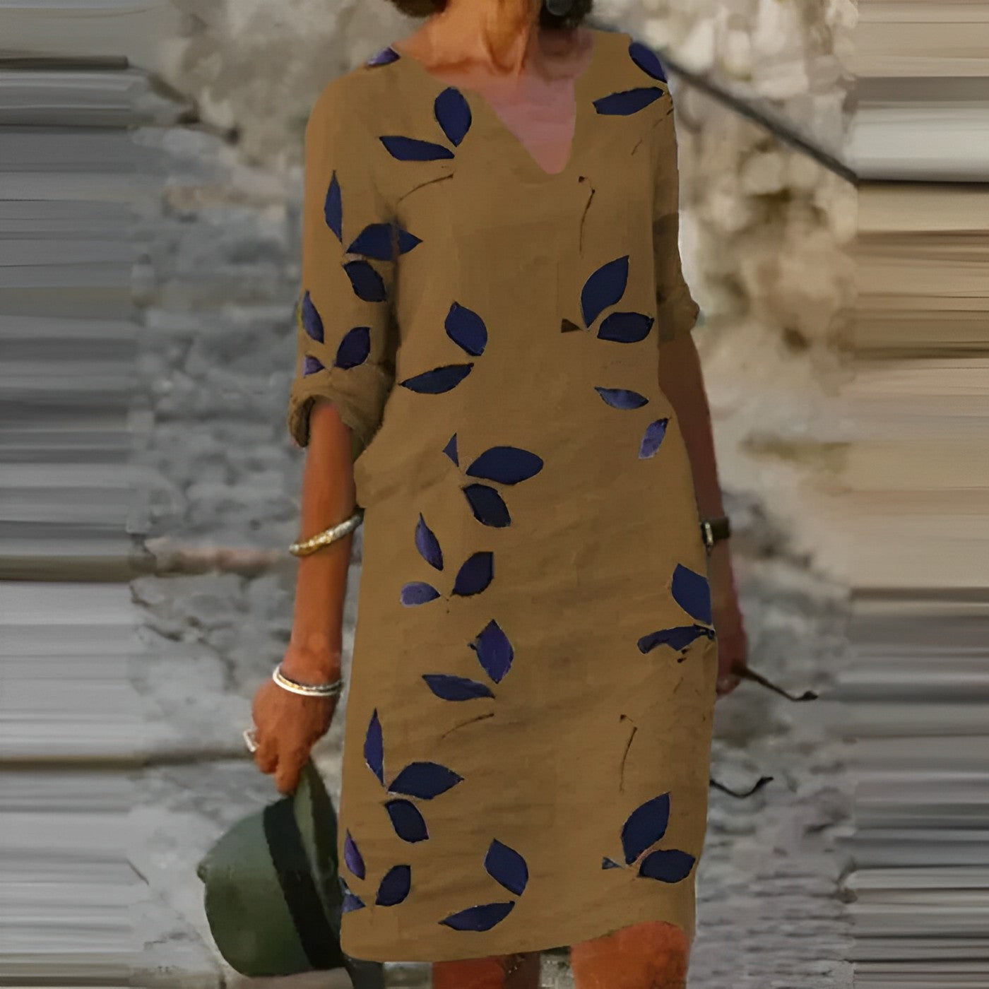 Woman wearing a brown dress with blue leaf patterns in an outdoor setting.