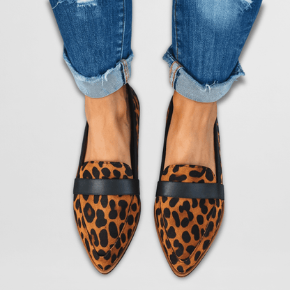 Leopard print loafers with black accents worn with rolled-up jeans on a light gray background