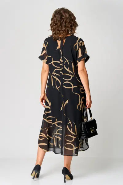 Woman wearing a black dress with gold patterns, holding a black handbag on a white background