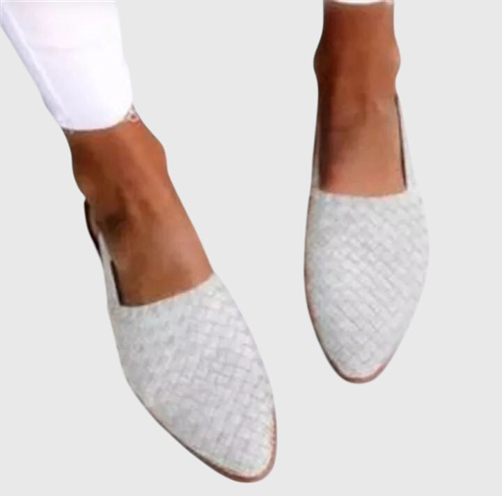 White woven flat shoes worn with white pants on a light gray background