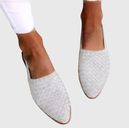 White woven flat shoes worn with white pants on a light gray background