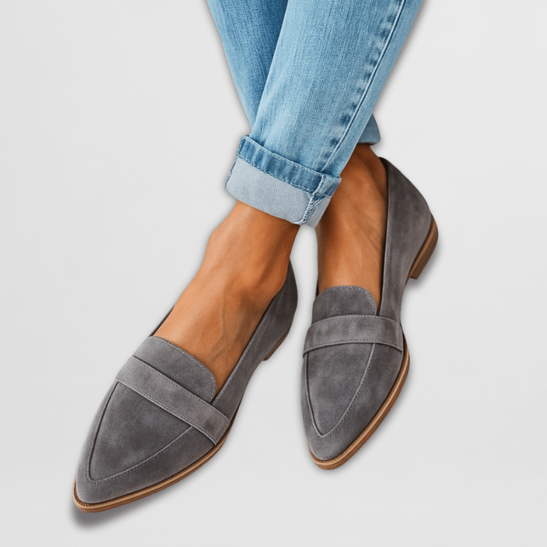 Gray suede loafers worn with rolled-up blue jeans on a light gray background