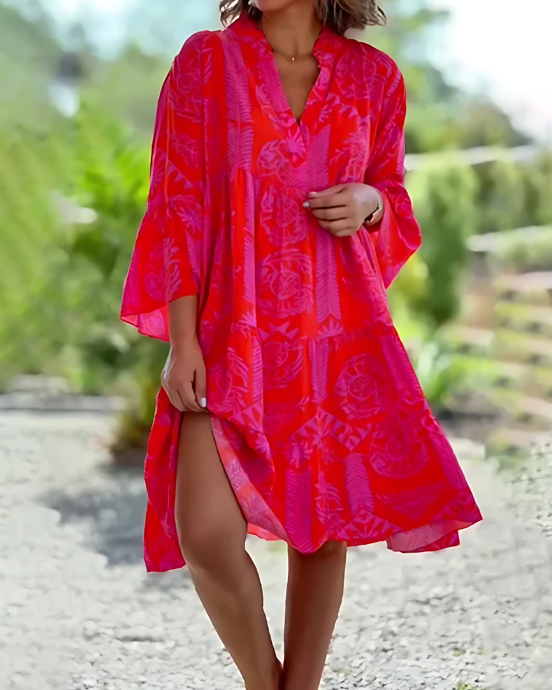 Woman wearing a bright pink patterned dress outdoors with greenery in the background