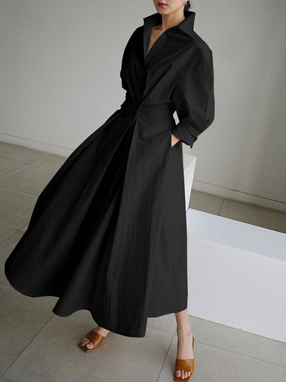 Person wearing a long black coat in a minimal indoor setting