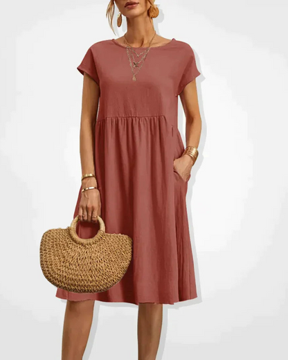 Woman wearing a rust-colored dress holding a woven bag on a white background
