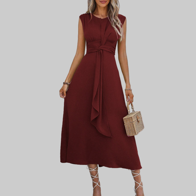 Woman wearing a burgundy dress holding a small handbag on a plain background
