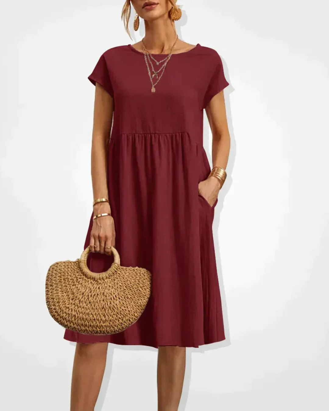Woman wearing a burgundy dress holding a straw bag on a white background