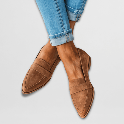 Brown loafers worn with rolled-up blue jeans on a light gray background