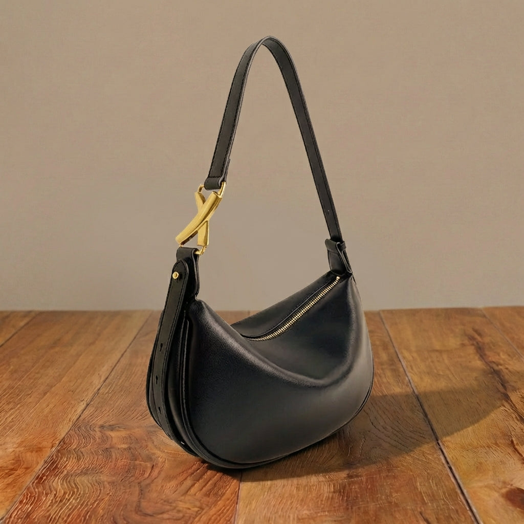 Black leather shoulder bag with a gold clasp on a wooden surface
