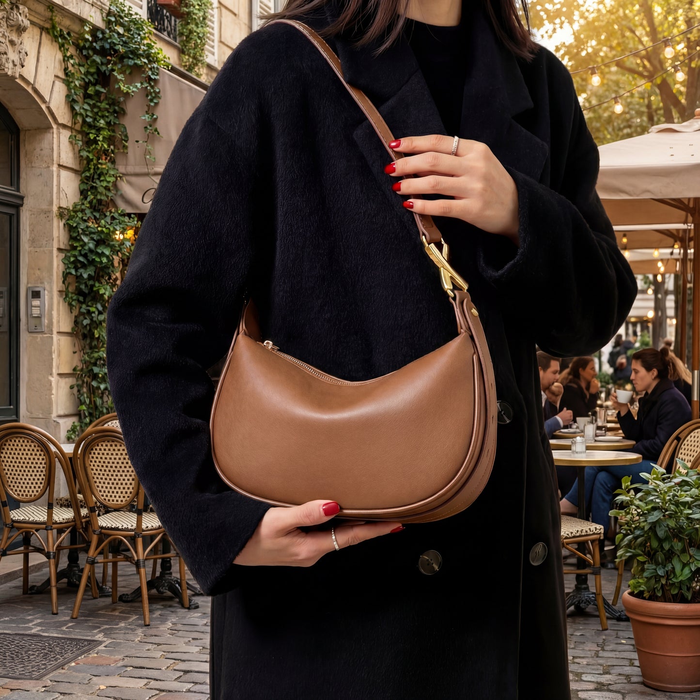 Person holding a brown leather small shoulder bag in an outdoor cafe setting