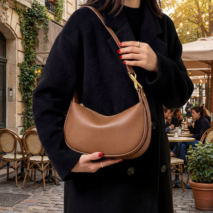 Person holding a brown leather small shoulder bag in an outdoor cafe setting