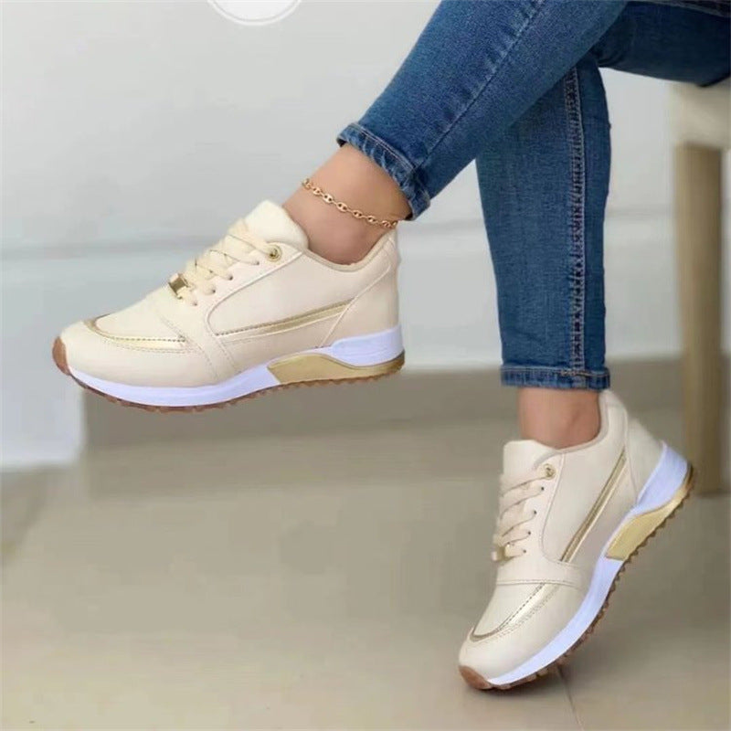 Beige sneakers with gold accents worn with blue jeans on a light background