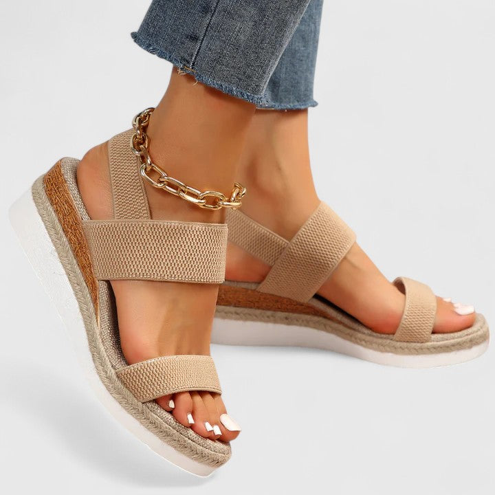 Beige wedge sandals with chain detail worn with blue jeans on a light gray background