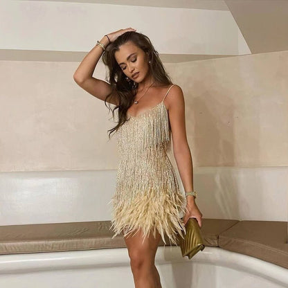 Woman in a beige fringe dress holding a gold clutch against a neutral background
