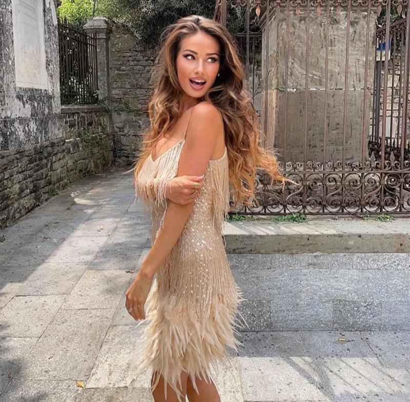 Woman in a beige fringe dress standing outdoors with stone steps and wall in the background