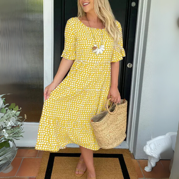 Woman in a yellow dress holding a straw bag, standing in front of a door.