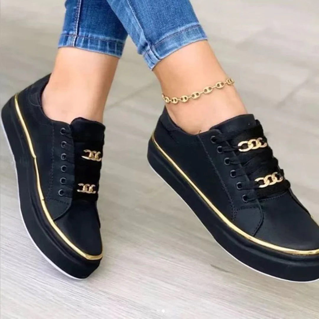 Black sneakers with gold accents worn by a person on a light gray background