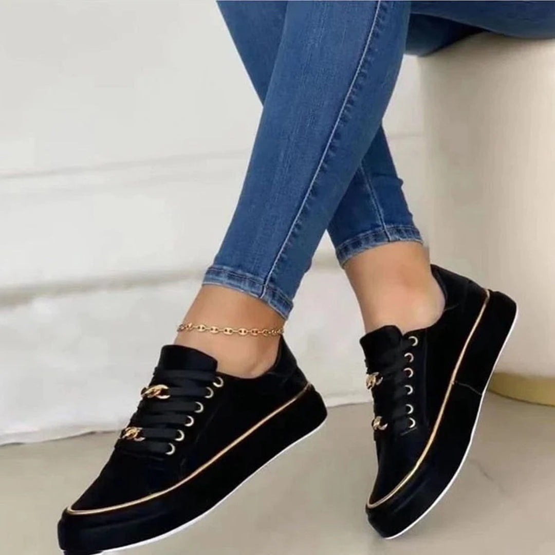 Black platform sneakers with gold accents worn with blue jeans on a white background