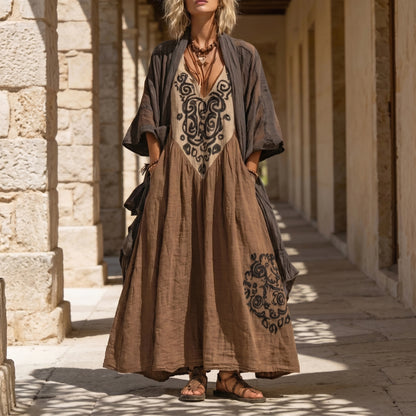 Woman wearing a long, embroidered brown dress in a sunlit stone corridor.