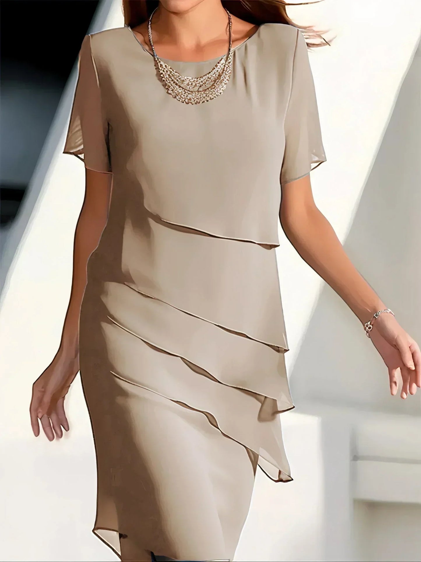 Beige dress with layered skirt and embellished neckline on a blurred background