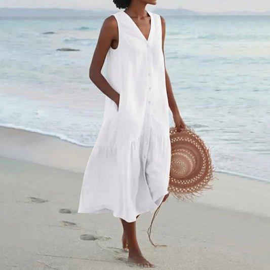 Woman in a white dress holding a straw hat on a beach