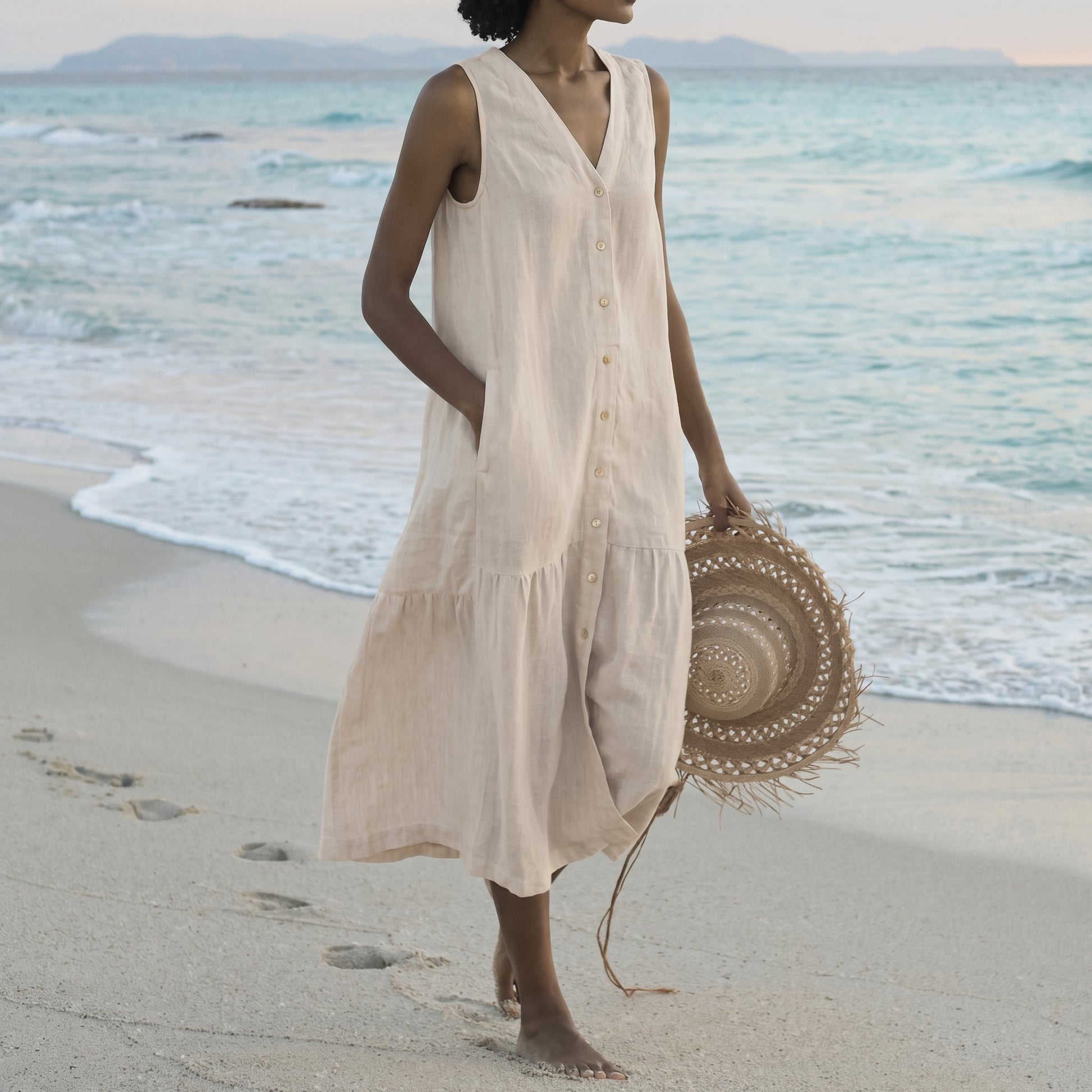 Woman in a beige dress holding a straw hat on a beach