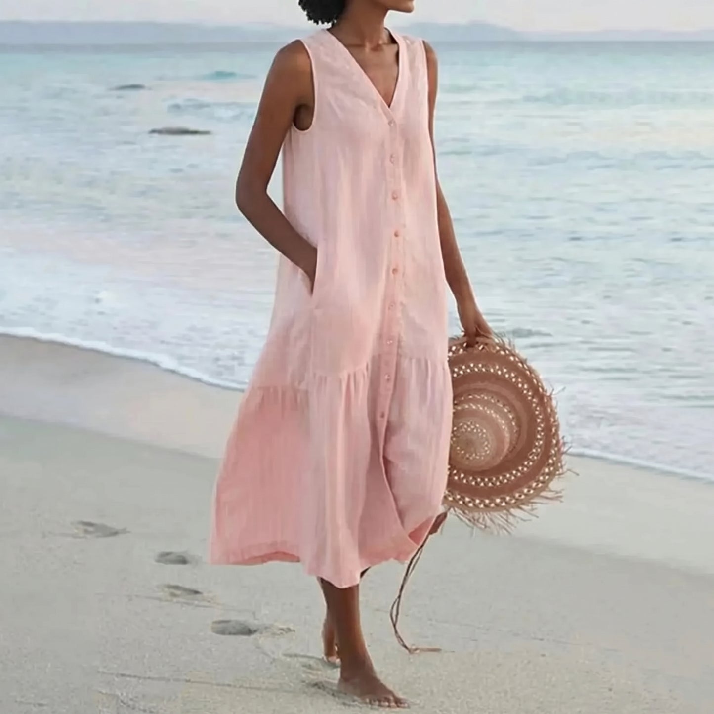 Woman in a pink dress holding a straw hat on a beach