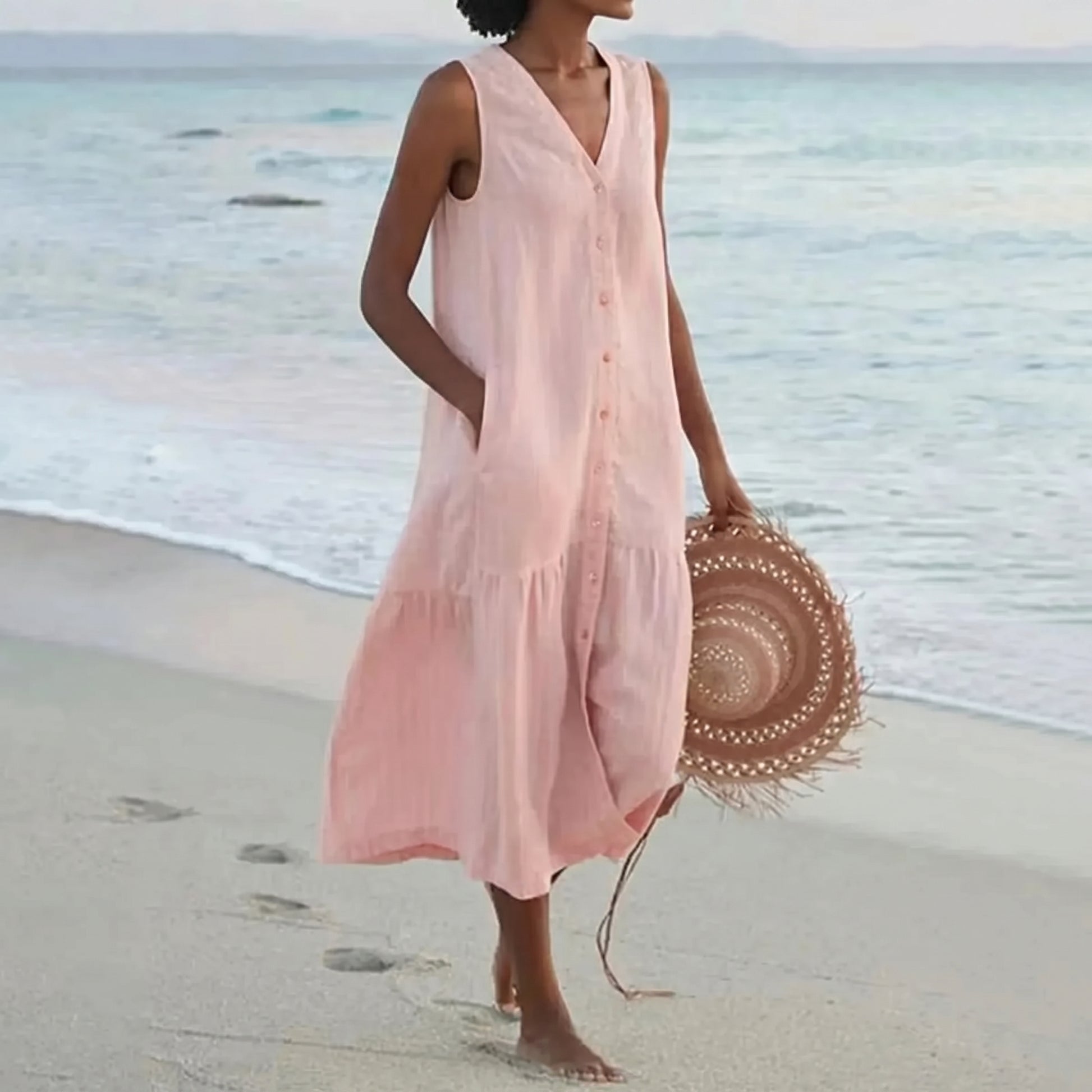 Woman in a pink dress holding a straw hat on a beach