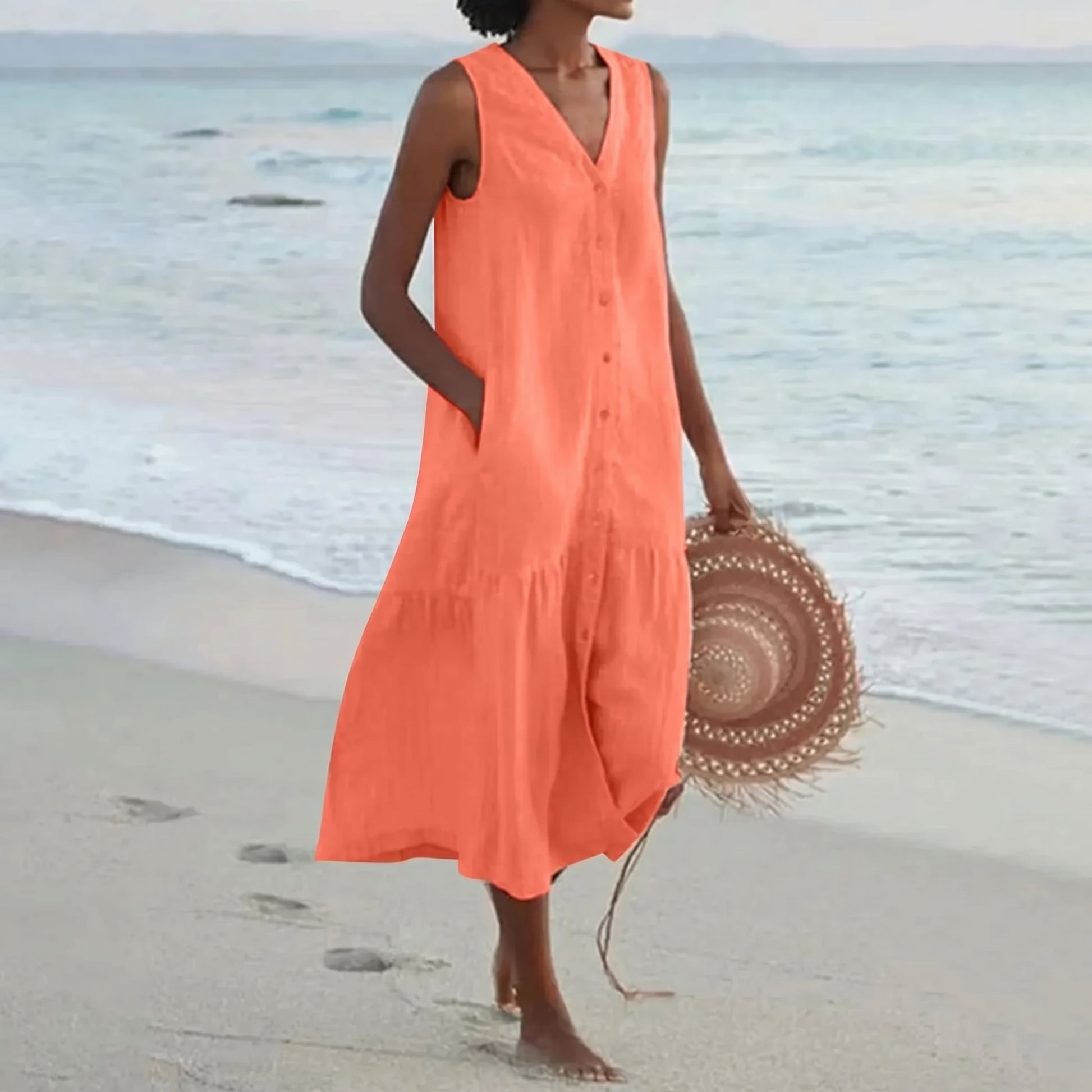 Woman in an orange dress holding a straw hat on a beach