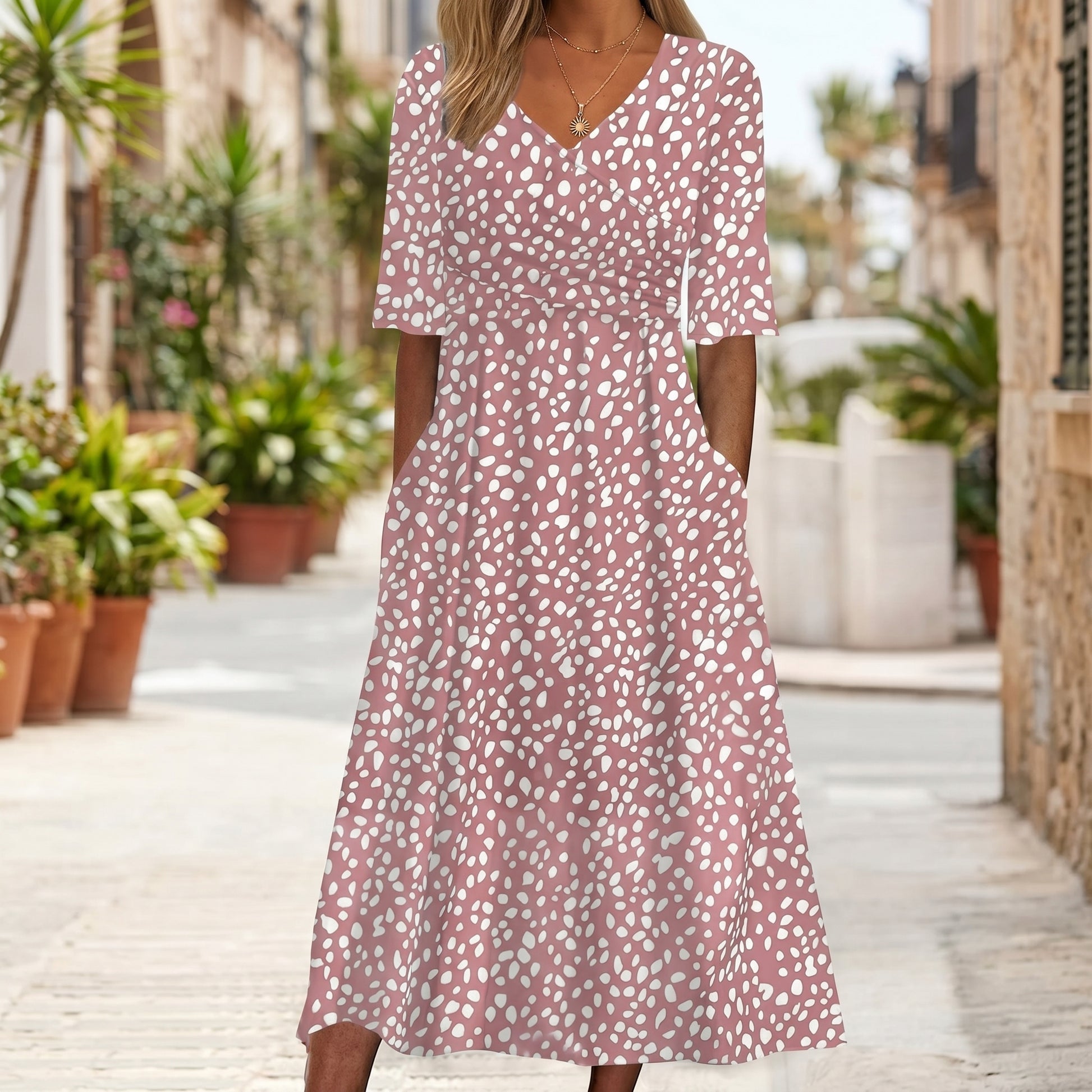 Woman wearing a pink floral dress standing on a street with plants and buildings in the background