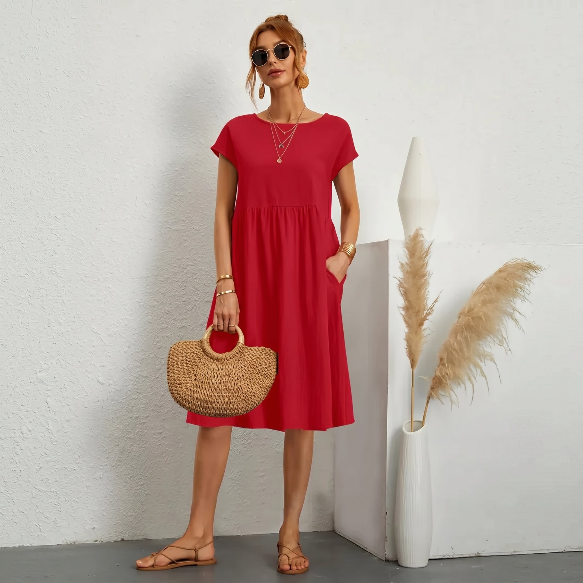 Woman in a red dress holding a straw bag against a white wall.