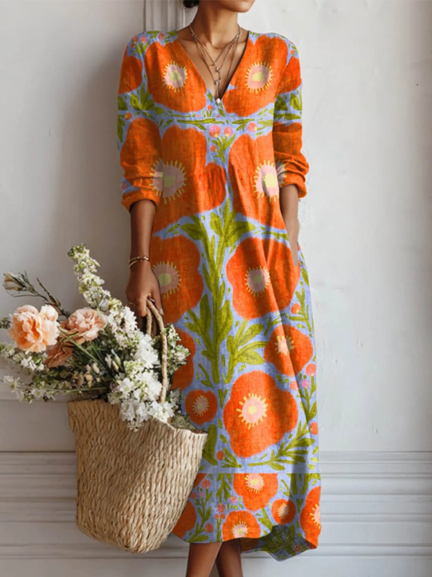 Woman wearing a colorful floral dress holding a woven bag with flowers against a white wall.