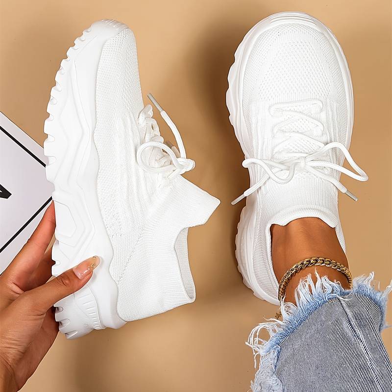 White sneakers being held by a hand with a beige background