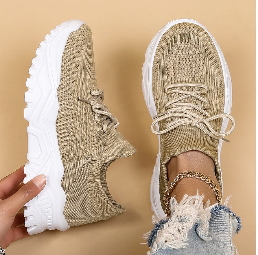 Beige sneakers with white soles worn by a person on a beige background