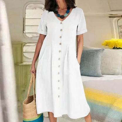 Woman wearing a white dress with buttons, holding a straw bag, in an indoor setting.