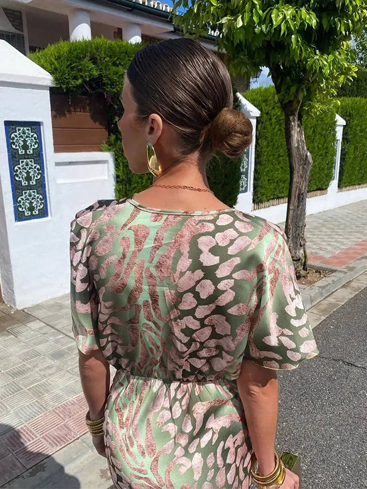 Woman wearing a patterned dress with a white building and greenery in the background