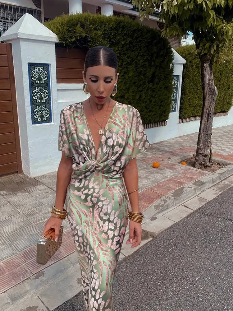 Woman in a floral dress standing on a sidewalk with a building and tree in the background