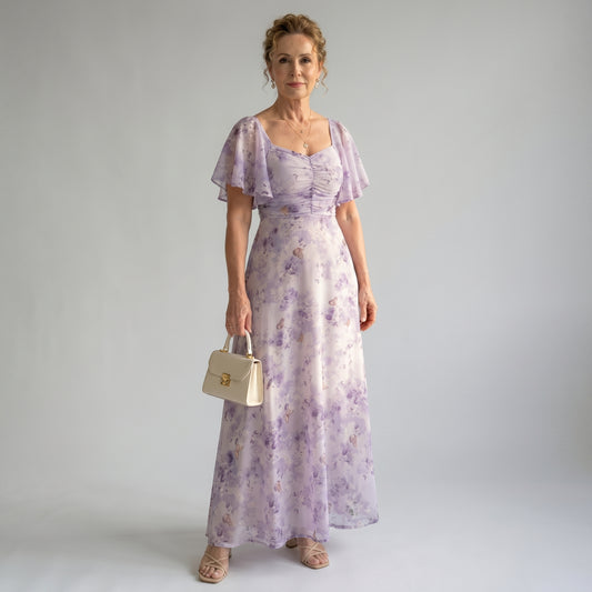 Woman wearing a purple floral dress holding a beige handbag against a plain background