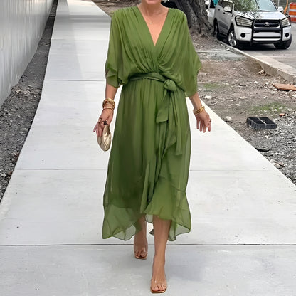 Woman in a green dress walking on a sidewalk with a street and vehicle in the background.