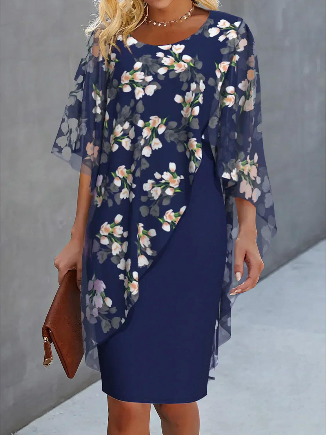 Woman wearing a navy blue dress with floral overlay against a gray background
