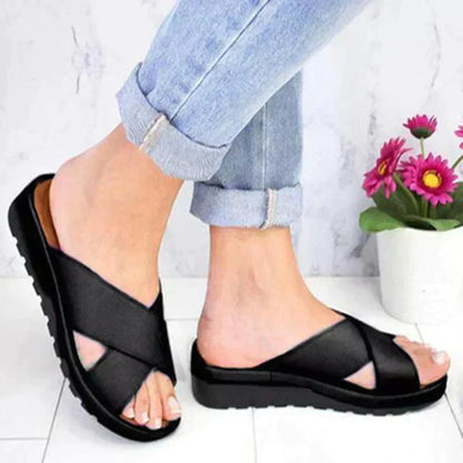 Black sandals worn with rolled-up jeans on a light wooden floor.