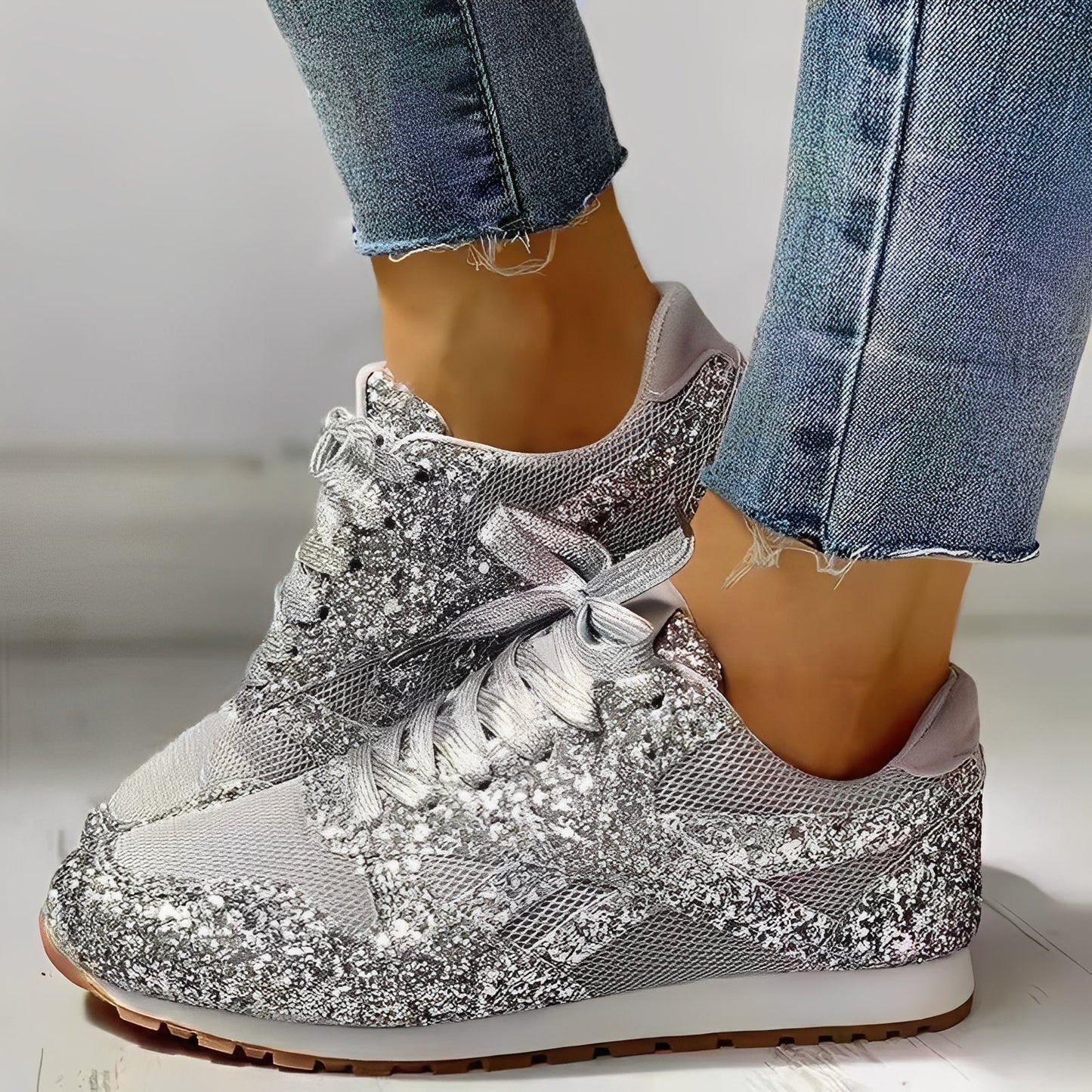 Silver glittery sneakers worn with blue jeans on a light background