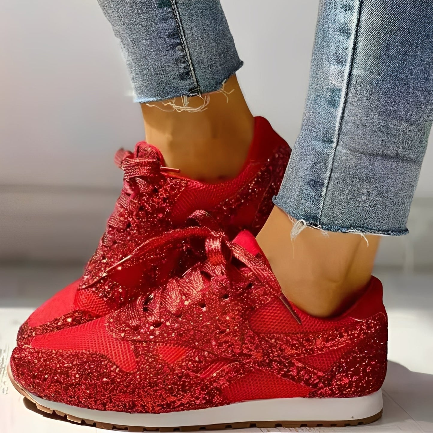 Red glittery sneakers worn with blue jeans on a neutral background