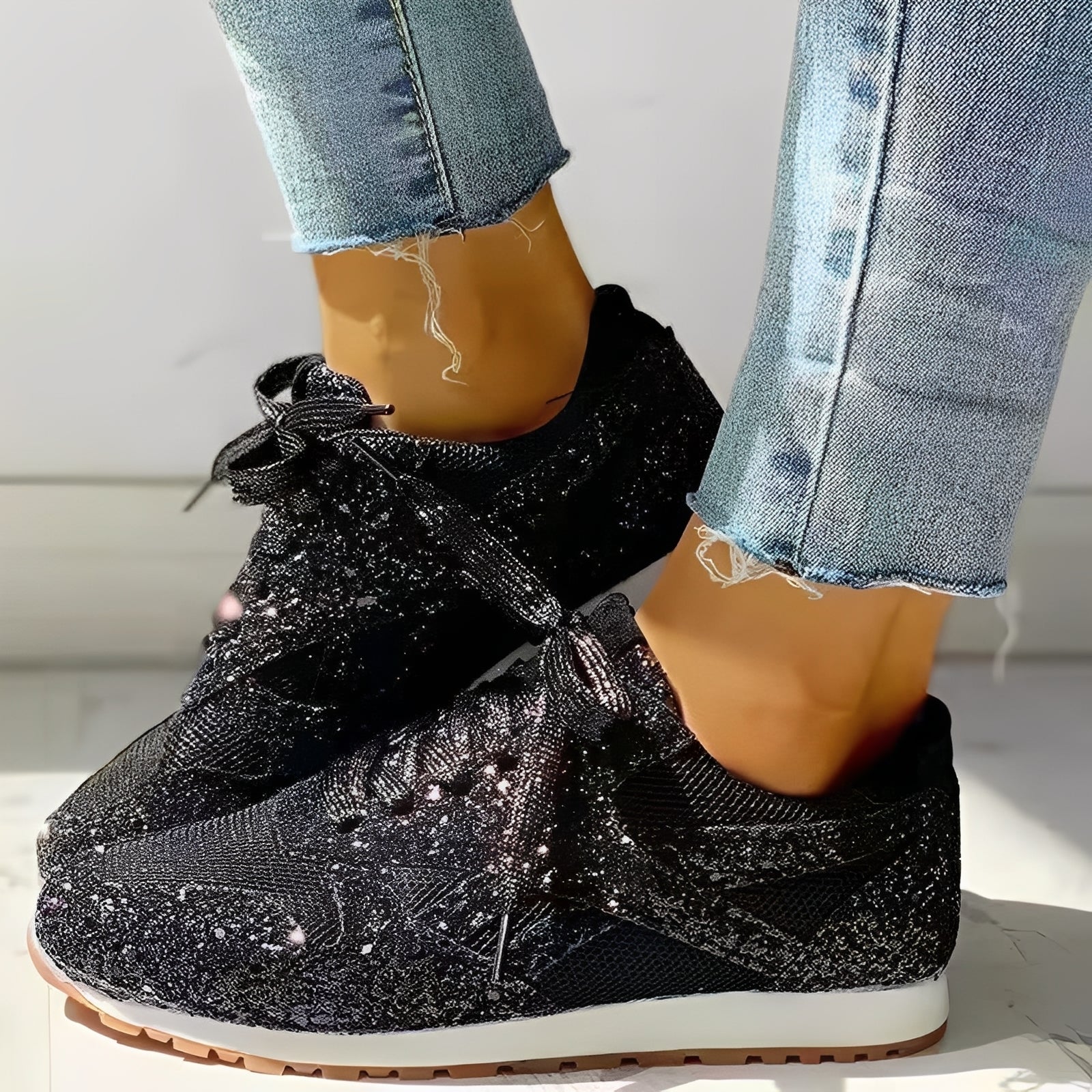 Black glittery sneakers worn with light blue jeans on a neutral background