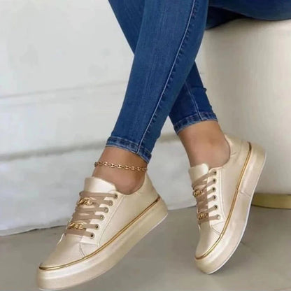 Beige sneakers with gold accents worn with blue jeans on a light background