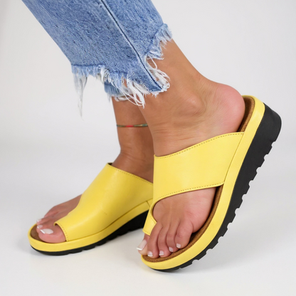Yellow sandals with black soles worn with light blue jeans on a white background