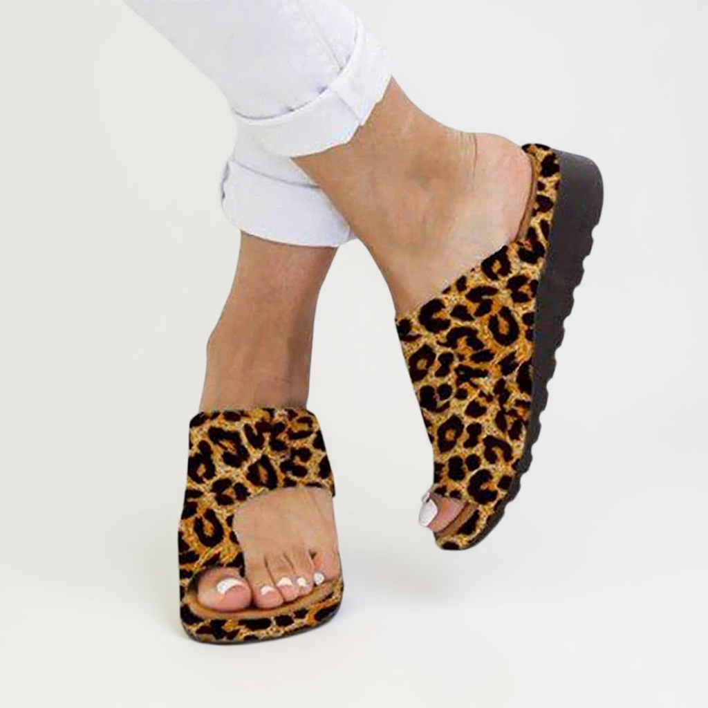 Leopard print sandals worn with white pants on a light gray background